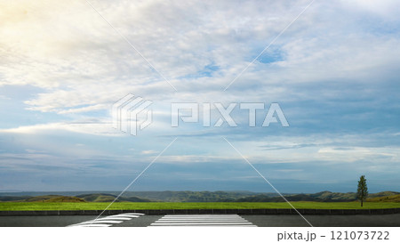 Asphalt street with pedestrian crosswalk and meadow field with blue sky and clouds in the background Asphalt street with pedestrian crosswalk and meadow field with blue sky and clouds in the background 121073722