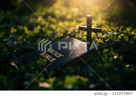 a bible book and a cross lying on the green clover leaves. 121073907