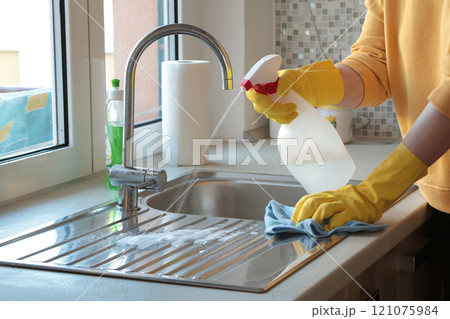 Woman in yellow rubber gloves wipes sink cleaner near window. House cleaning. Interior and kitchen. Woman in yellow rubber gloves wipes sink cleaner near window. House cleaning. Interior and kitchen. 121075984