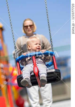 Mother pushing her infant baby boy child on a swing on playground outdoors Mother pushing her infant baby boy child on a swing on playground outdoors 121077720