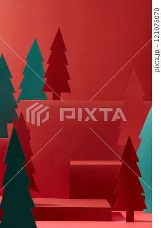 A frontal view of red cube podiums with empty space for product showcase, decorated by paper Noel trees with different sizes and colors, suitable for the Christmas concept in a crimson backdrop. 121078070