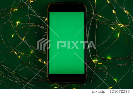 The phone lies horizontally with a green chromakey screen against a garland of yellow and green lights on a green background. High quality photo 121078236