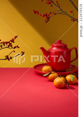 On a yellow backdrop, a close-up of a crimson display product table decorated by winterberry branches, a red teapot, and a red dish of tangerines. A template image with an idea of the Chinese New Year 121078319
