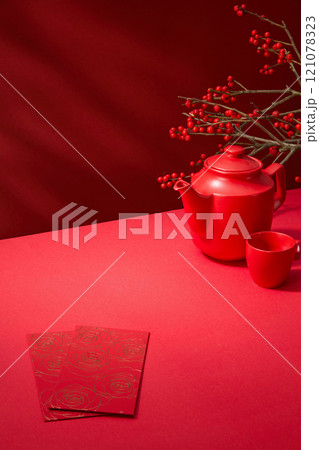 An Asian New Year table is decorated with a teapot, red envelopes, and a winterberry tree against a red backdrop, while there is a blank space for a products display. Template photo with a high angle. An Asian New Year table is decorated with a teapot, red envelopes, and a winterberry tree against a red backdrop, while there is a blank space for a products display. Template photo with a high angle. 121078323