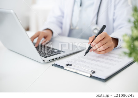 A close-up of a doctor working at her desk, typing on the laptop keyboard, reading medical paper. A close-up of a doctor working at her desk, typing on the laptop keyboard, reading medical paper. 121080245