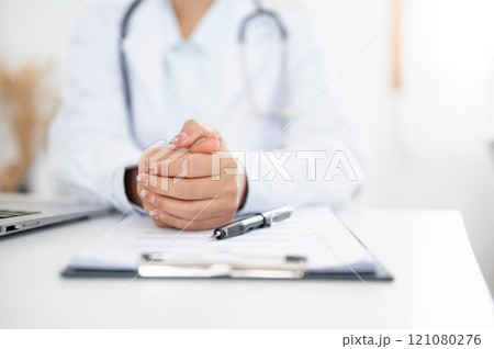 A doctor sitting at her desk with her hands clasped together, displaying a serious expression. A doctor sitting at her desk with her hands clasped together, displaying a serious expression. 121080276