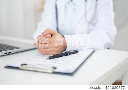 A doctor sitting at her desk with her hands clasped together, displaying a serious expression. A doctor sitting at her desk with her hands clasped together, displaying a serious expression. 121080277