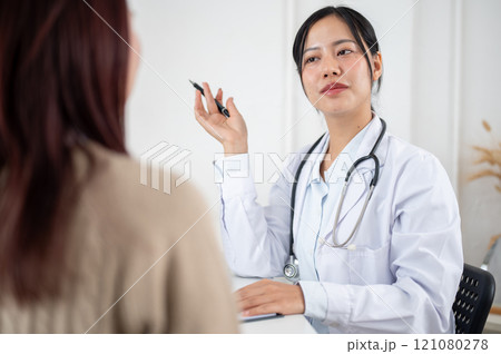 A doctor working in the examination room, listening to a patient describing their symptoms. A doctor working in the examination room, listening to a patient describing their symptoms. 121080278