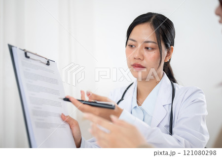 A doctor showing a medical paper to a patient while discussing the treatment plan at the hospital. 121080298