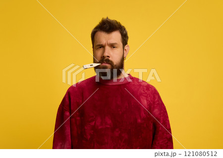 Portrait of young man with beard, with thermometer in mouth, measuring temperature against bright yellow background. Viruses and symptoms. 121080512