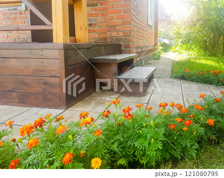 Close-up of a brown wooden porch with steps near a red brick wall in a rustic country house, on a sunny summer day Close-up of a brown wooden porch with steps near a red brick wall in a rustic country house, on a sunny summer day 121080795