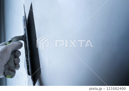 Worker uses a trowel to apply epoxy adhesive on a wall for repair. 121082400