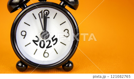 Business concept of 2025 new year symbol. Beautiful orange paper with number 2025. Beautiful orange background, copy space. Black alarm clock. Business 2025 happy new year concept. 121082765