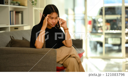 Frustrated young woman talking mobile phone while sitting on the sofa Frustrated young woman talking mobile phone while sitting on the sofa 121083796