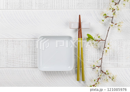 Table adorned with cherry blossom branch and chopsticks, epitomizing Japanese food culture 121085976