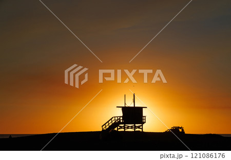 Los Angeles beach at sunset, featuring a lifeguard tower silhouette against a glowing orange and purple horizon Los Angeles beach at sunset, featuring a lifeguard tower silhouette against a glowing orange and purple horizon 121086176