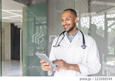 Professional doctor using a tablet for medical records in a bright, contemporary workspace. This picture conveys concepts of healthcare, technology, and professionalism in a modern medical setting. Professional doctor using a tablet for medical records in a bright, contemporary workspace. This picture conveys concepts of healthcare, technology, and professionalism in a modern medical setting. 121088544