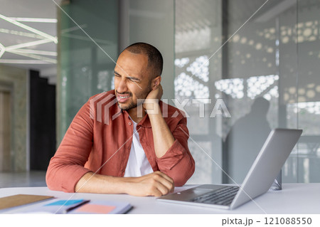 Man holding neck in discomfort at office desk with laptop. Depicts workplace ergonomics, stress, and physical strain. Ideal for illustrating office-related health issues and computer overuse. Man holding neck in discomfort at office desk with laptop. Depicts workplace ergonomics, stress, and physical strain. Ideal for illustrating office-related health issues and computer overuse. 121088550