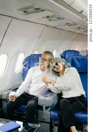 Smiling senior couple of Asian tourists take photos of each other while sitting on a plane. with digital tablet, laptop and smartphone. Travel in style, Smiling senior couple of Asian tourists take photos of each other while sitting on a plane. with digital tablet, laptop and smartphone. Travel in style, 121088819