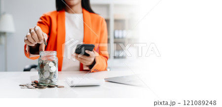 Saving money with hand putting coins in jug glass and calculator to calculate budget concept finance and accounting Saving money with hand putting coins in jug glass and calculator to calculate budget concept finance and accounting 121089248