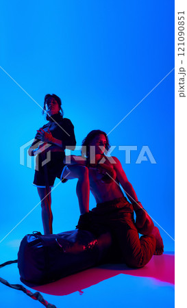 Portrait of shirtless man and woman in sportswear, wearing boxing gloves, posing against blue studio background in neon light. Full-length Portrait of shirtless man and woman in sportswear, wearing boxing gloves, posing against blue studio background in neon light. Full-length 121090851
