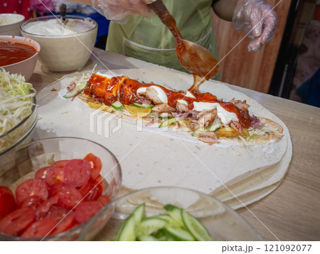 【ウクライナ】東部ドニプロ市内の屋台でシュワルマ生地の上に並べられた野菜や肉にソースをかける人 121092077