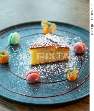Slice of lemon cake with icing sugar served on a plate with macarons and physalis Slice of lemon cake with icing sugar served on a plate with macarons and physalis 121092597