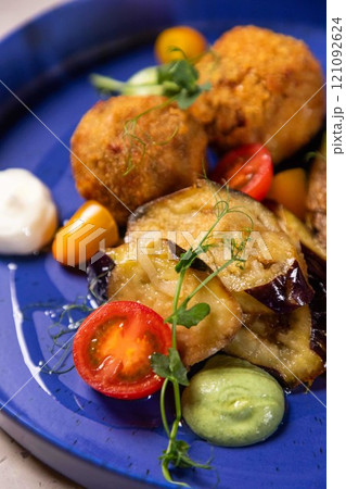 Arancini being served on blue plate with eggplant and tomatoes Arancini being served on blue plate with eggplant and tomatoes 121092624