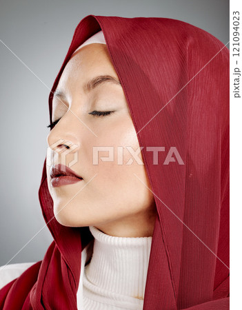 Closeup of a glowing beautiful muslim woman with eyelash extensions isolated against grey background in studio. Young woman wearing a red hijab or headscarf and jewellery. Perfect and flawless skin Closeup of a glowing beautiful muslim woman with eyelash extensions isolated against grey background in studio. Young woman wearing a red hijab or headscarf and jewellery. Perfect and flawless skin 121094023