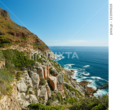 Landscape view of mountains surrounded by ocean in Hout Bay in Cape Town, South Africa. Beautiful popular tourist attraction of scenic hills and calm blue water. Exploring nature and the wild 121094026