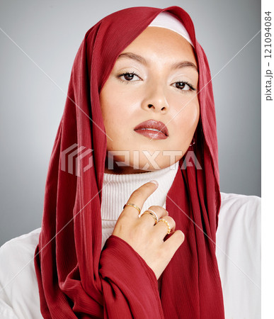 Portrait of a Muslim woman wearing a red hijab or headscarf showing her eyelash extensions and makeup. Showing her flawless skin glowing. Beautiful woman isolated against a grey studio background. 121094084
