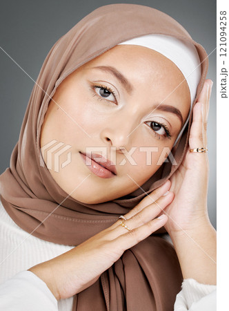 Portrait of a glowing elegant muslim womans face isolated against grey studio background. Young woman wearing a hijab or headscarf, showing her eyelash extensions, jewellery and skin routine Portrait of a glowing elegant muslim womans face isolated against grey studio background. Young woman wearing a hijab or headscarf, showing her eyelash extensions, jewellery and skin routine 121094258