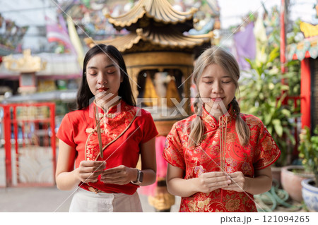 Celebrating chinese new year two women in traditional attire temple setting cultural ritual vibrant atmosphere close-up perspective 121094265