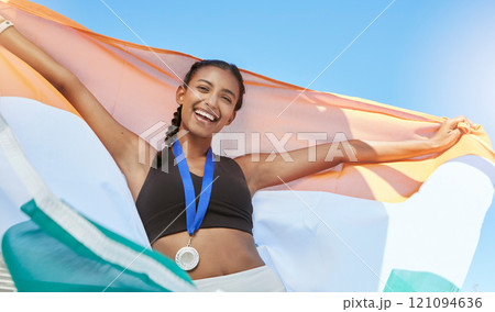 Portrait of a young fit indian female athlete cheering and holding India flag after competing in sports. Smiling fit active sporty woman feeling motivated and celebrating 121094636