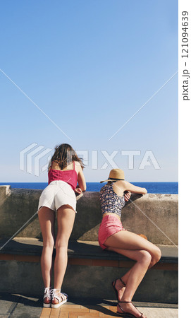 Beach, promenade and back of women with view for outdoor adventure, vacation and sightseeing together. Summer, peace and female friends watching ocean by concrete for travel, holiday and tourism 121094639
