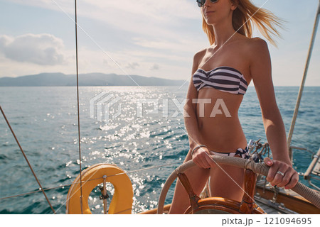 Woman, bikini and yacht with hands on steering wheel, outdoor and travel in sunshine on ocean. Girl, boat and summer with swimwear, direction and control on cruise, holiday and journey in Italy Woman, bikini and yacht with hands on steering wheel, outdoor and travel in sunshine on ocean. Girl, boat and summer with swimwear, direction and control on cruise, holiday and journey in Italy 121094695