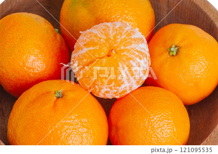 Peeled and unpeeled tangerines in a wooden plate. Citrus fruits tangerines. 121095535