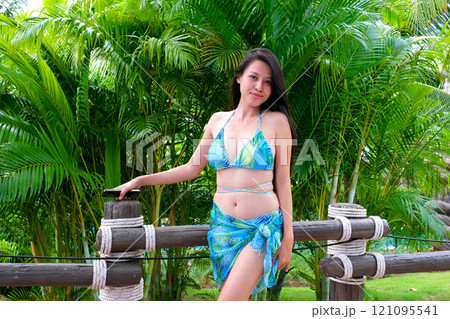 Young attractive hispanic woman in summer attire with a straw hat and floral lei posing against a vibrant background 121095541