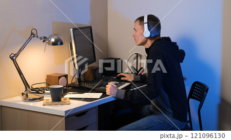 Young man immersed in creating music in his home studio, utilizing a MIDI keyboard and a PC, showcasing his passion and creativity during an evening session 121096130