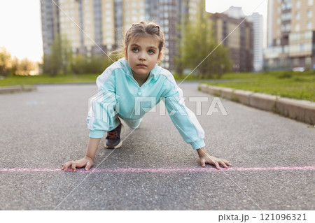 serious girl 7 years old primary school student in sports clothes took stand at starting position on street on road outdoor 121096321