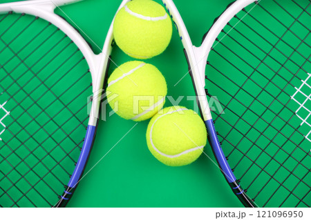 Two lawn tennis rackets lie next to each other on a green background, with yellow tennis balls between them. High quality photo Two lawn tennis rackets lie next to each other on a green background, with yellow tennis balls between them. High quality photo 121096950