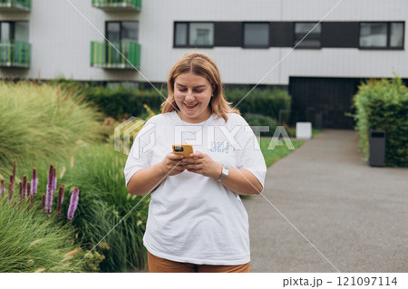 Smiling woman text messaging on smart phone at sunny day. Urban lifestyle concept. Happy woman chatting on phone and relaxing outdoors. 121097114