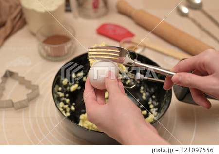 Christmas homemade baking, ingredients for baking gingerbread, woman fork breaks an egg in black bowl Christmas homemade baking, ingredients for baking gingerbread, woman fork breaks an egg in black bowl 121097556