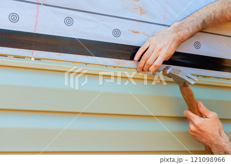 Craftsperson installing siding using hammer careful techniques on residential building in vinyl siding broad Craftsperson installing siding using hammer careful techniques on residential building in vinyl siding broad 121098966
