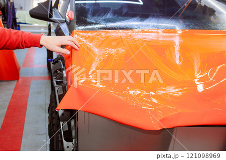 Technician wraps vehicle in bright orange vinyl at an auto customization shop. 121098969