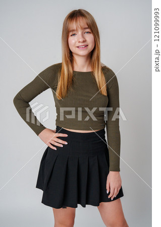 A young woman with straight hair wearing a green top poses against a neutral background A young woman with straight hair wearing a green top poses against a neutral background 121099993