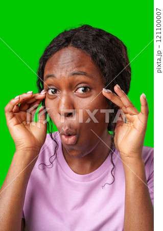 Surprised woman expressing shock while posing with hands on her face against a bright green backdrop Surprised woman expressing shock while posing with hands on her face against a bright green backdrop 121100007