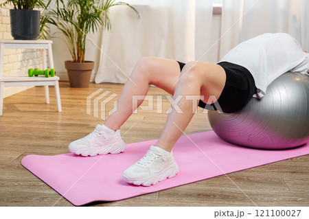 Young woman exercising on a stability ball in a bright room with plants 121100027
