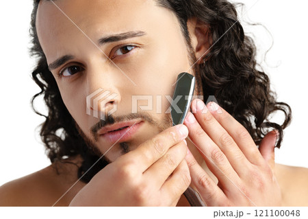 Man with curly hair grooming his beard carefully using a straight razor against a plain white background Man with curly hair grooming his beard carefully using a straight razor against a plain white background 121100048