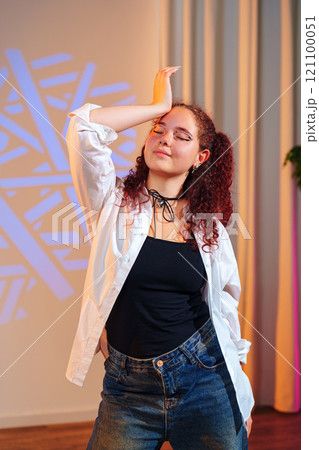 A young woman with red curly hair poses in a white shirt and blue jeans 121100051